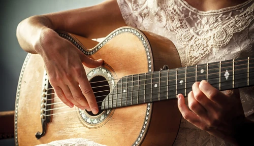 En person med spetstopp spelar på en akustisk gitarr, med ena handen på strängarna och den andra på bandet. Bilden fokuserar på händerna och gitarren.
